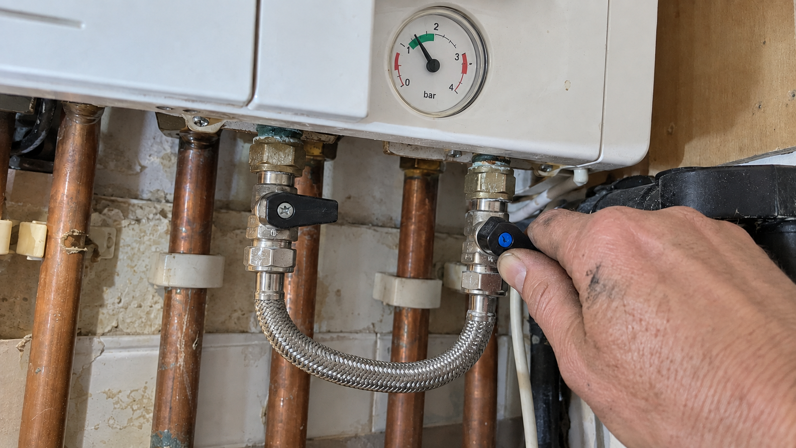 Hand operating a boiler filling loop beside a visible pressure gauge